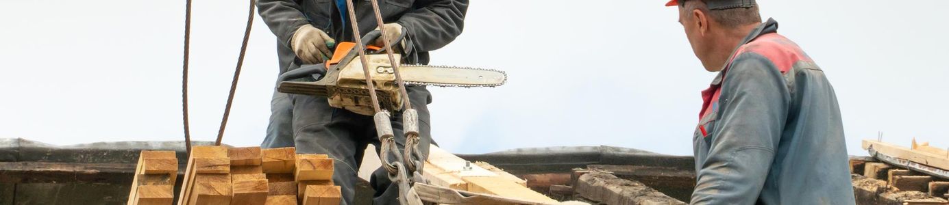 Tapasztalt ács mester és tetőfedő ács - minőségi ácsmunka családi ház tetőjén. Tapasztalt ács mester és tetőfedő ács dolgozik egy családi ház tetőszerkezetén, szakszerű ácsmunka közben.